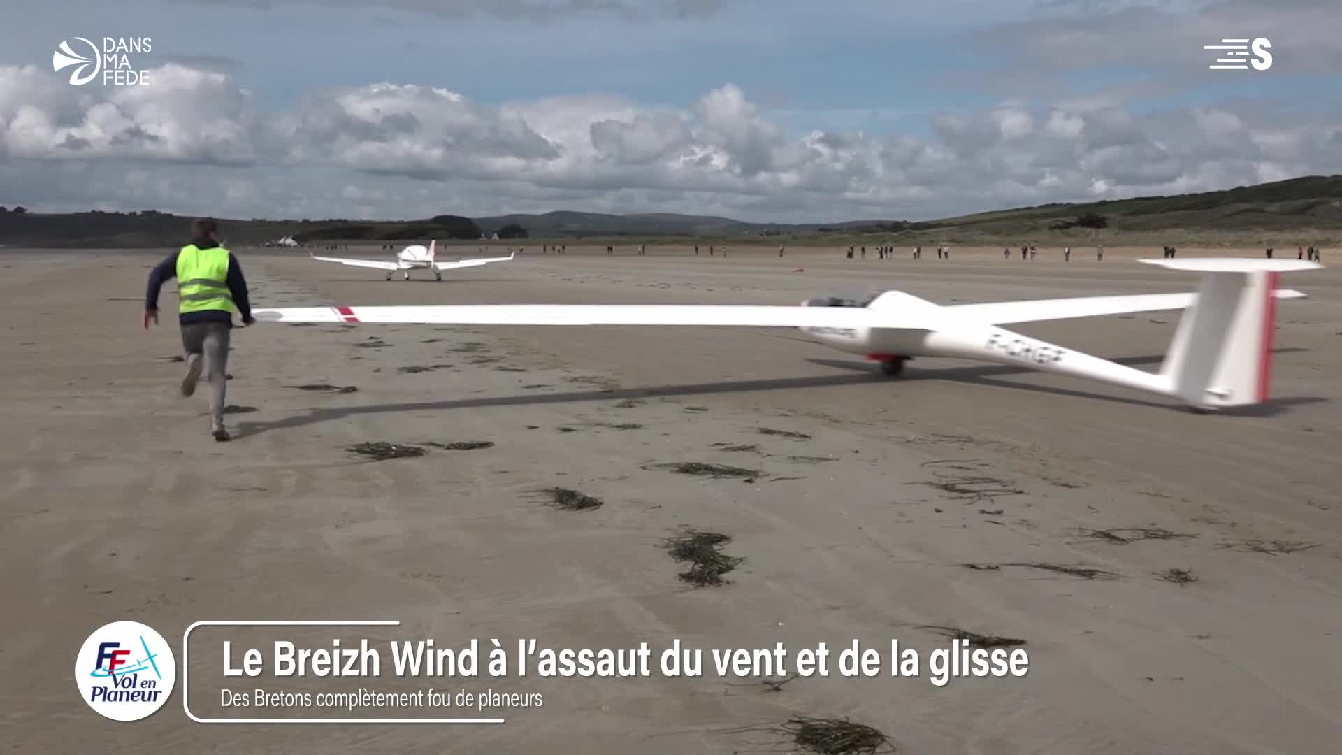 A glider with long, white wings is rolling across the sand, the red and white tail fin visible. A man in a bright vest sprints alongside it, presumably helping with the launch on this beach in France, as seen on Sport en France.

