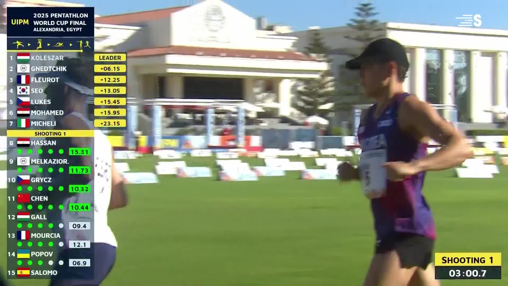 A competitor in a purple and black uniform strides across the grass, his face set in concentration. The scoreboard, with the Sport en France logo, shows the running order for the pentathlon event.
