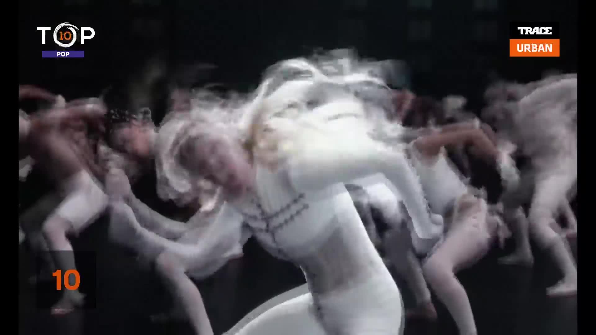 Dancers in white costumes are blurred by the rapid movement, their limbs outstretched as they move across the stage. The Trace Urban logo is visible, and it's the tenth song on the Top 10 Pop chart.
