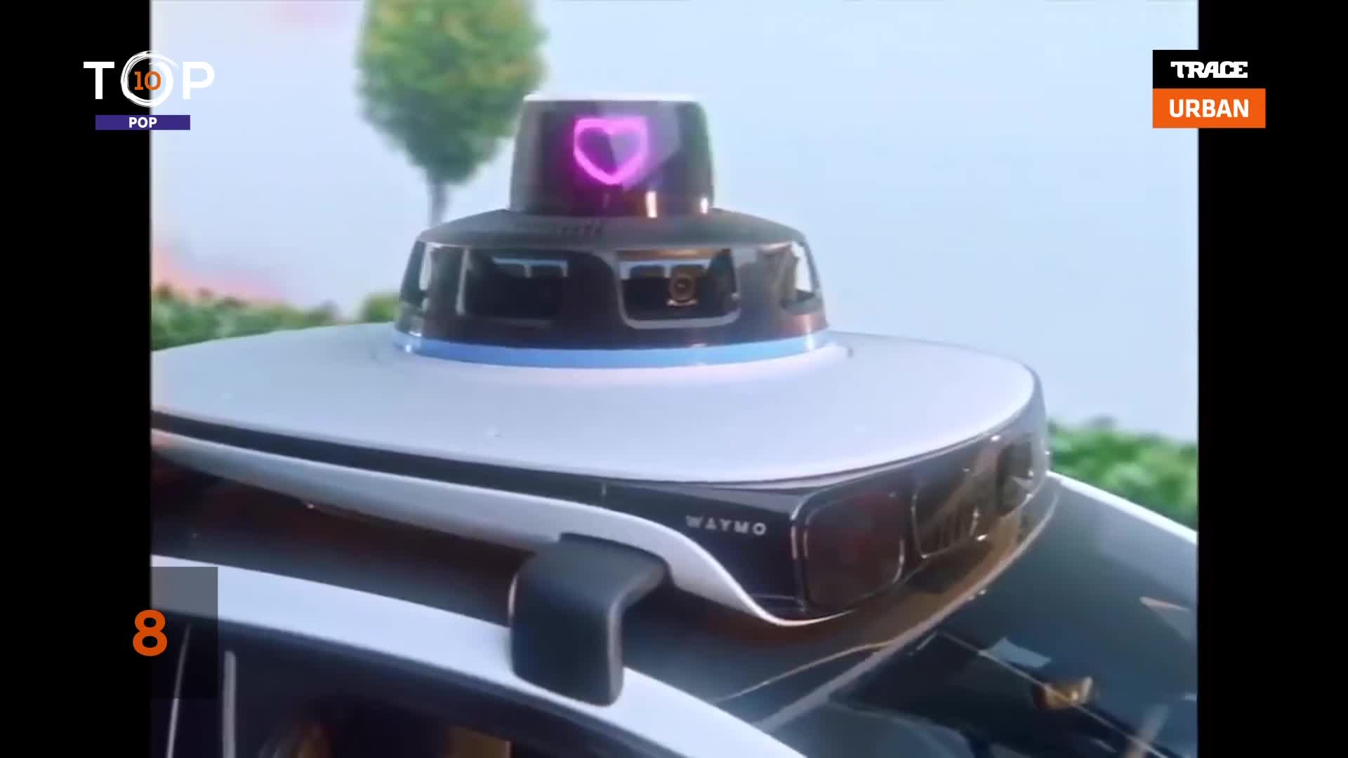 A Waymo vehicle's sensor array, topped with a glowing purple heart, is the focus. The scene is likely part of a segment from Trace Urban, a French music channel.
