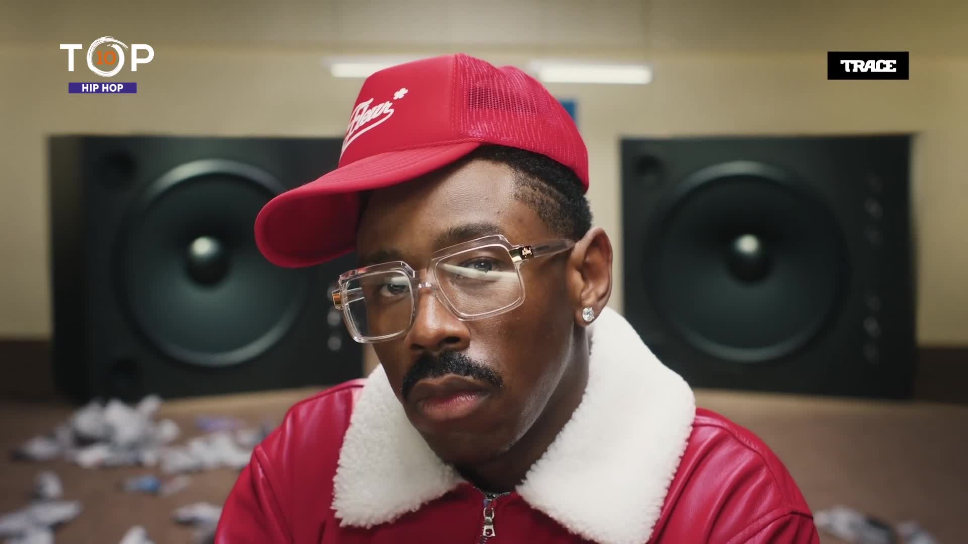 The man in the red jacket and cap stares directly ahead, framed by giant speakers. The Trace Urban logo is visible, and the Top Hip Hop logo is in the corner.
