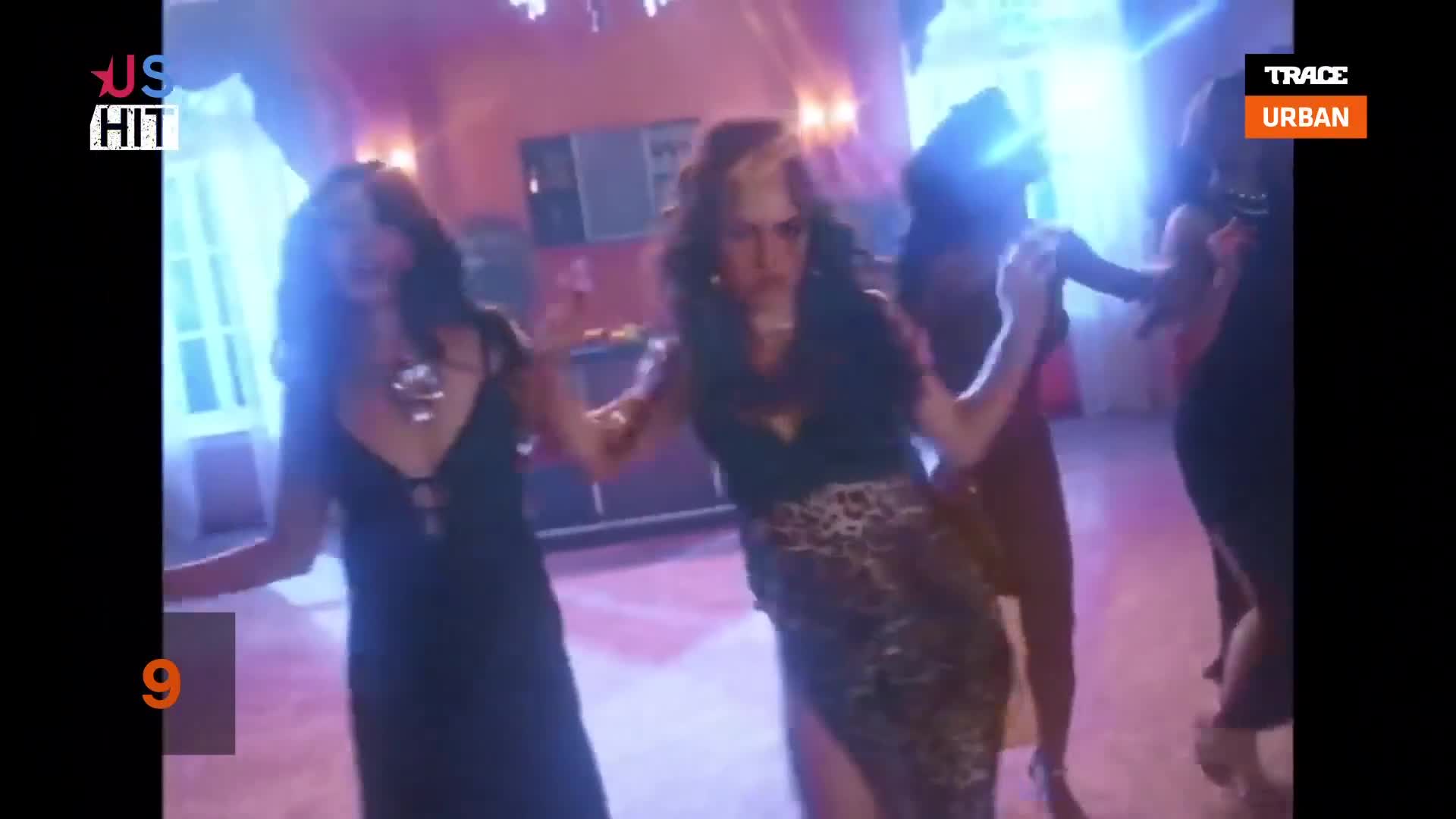 The women are dancing, their arms linked, moving in a circle. A leopard-print skirt catches the light as one woman spins.
