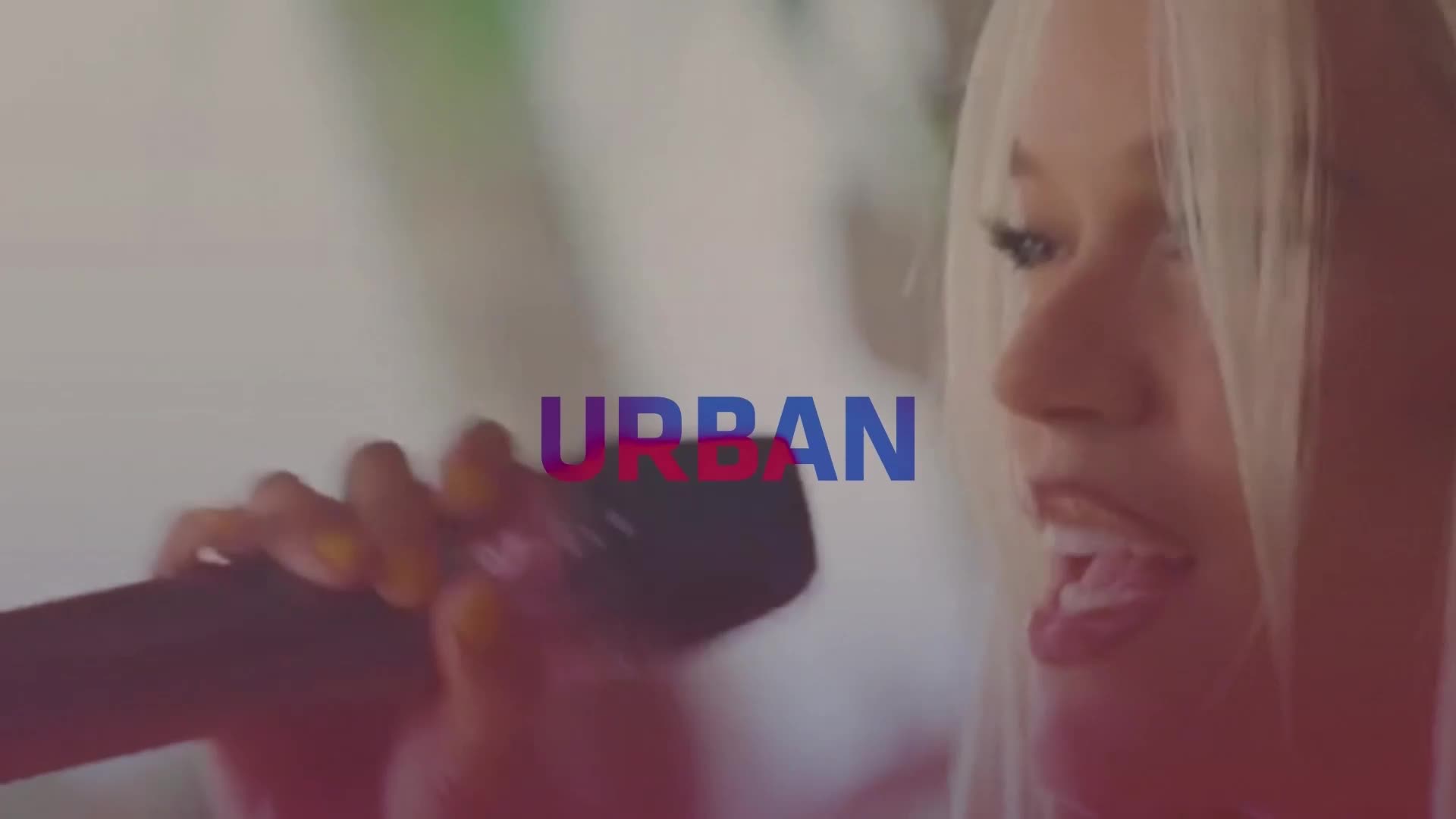 A blonde woman with a microphone is singing, her mouth wide open, as the word "URBAN" floats in front of her. The scene, likely from a music video, has a pink and blue color scheme, and the logo suggests it's on the French music channel, Trace Urban.
