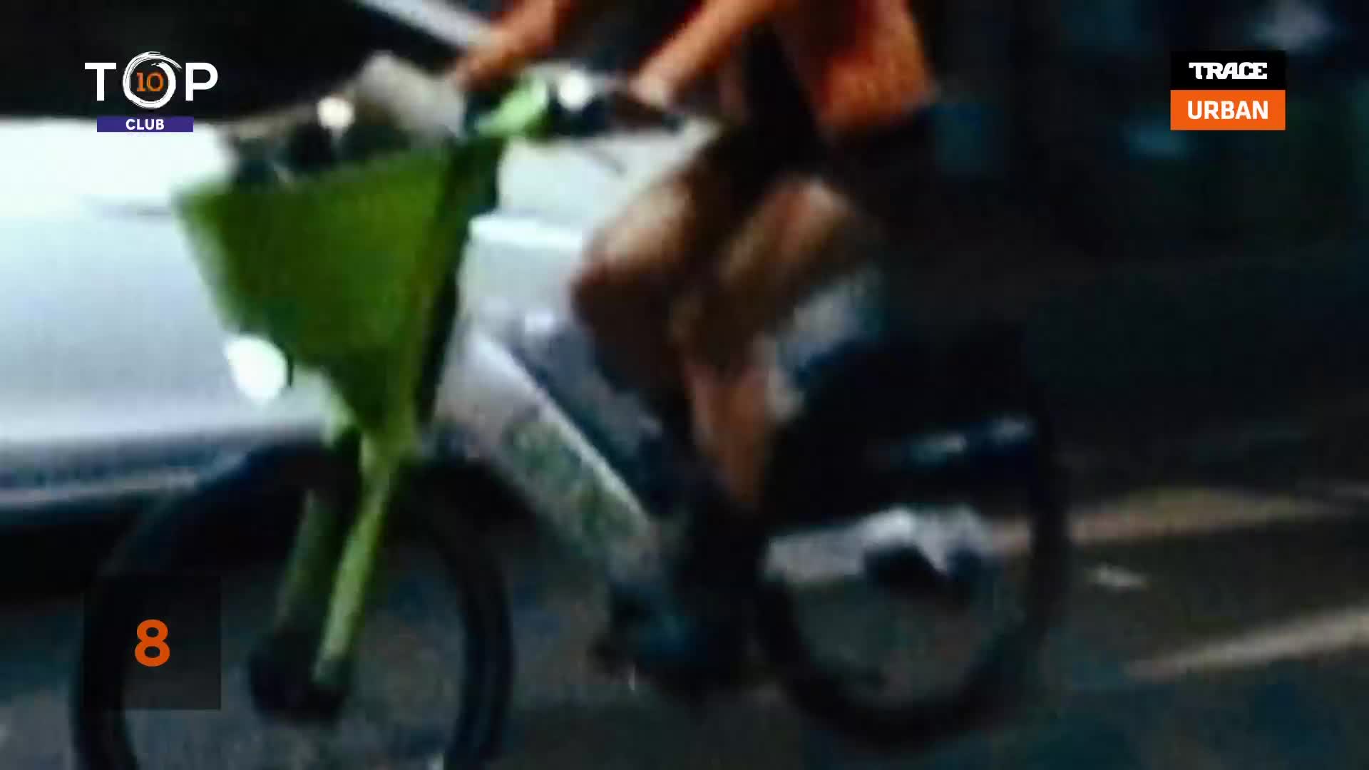 A person pedals a bright green Lime bike, the front basket illuminated by a headlight. The scene looks like it's from a music video on Trace Urban, with a "Top 10 Club" graphic in the corner.
