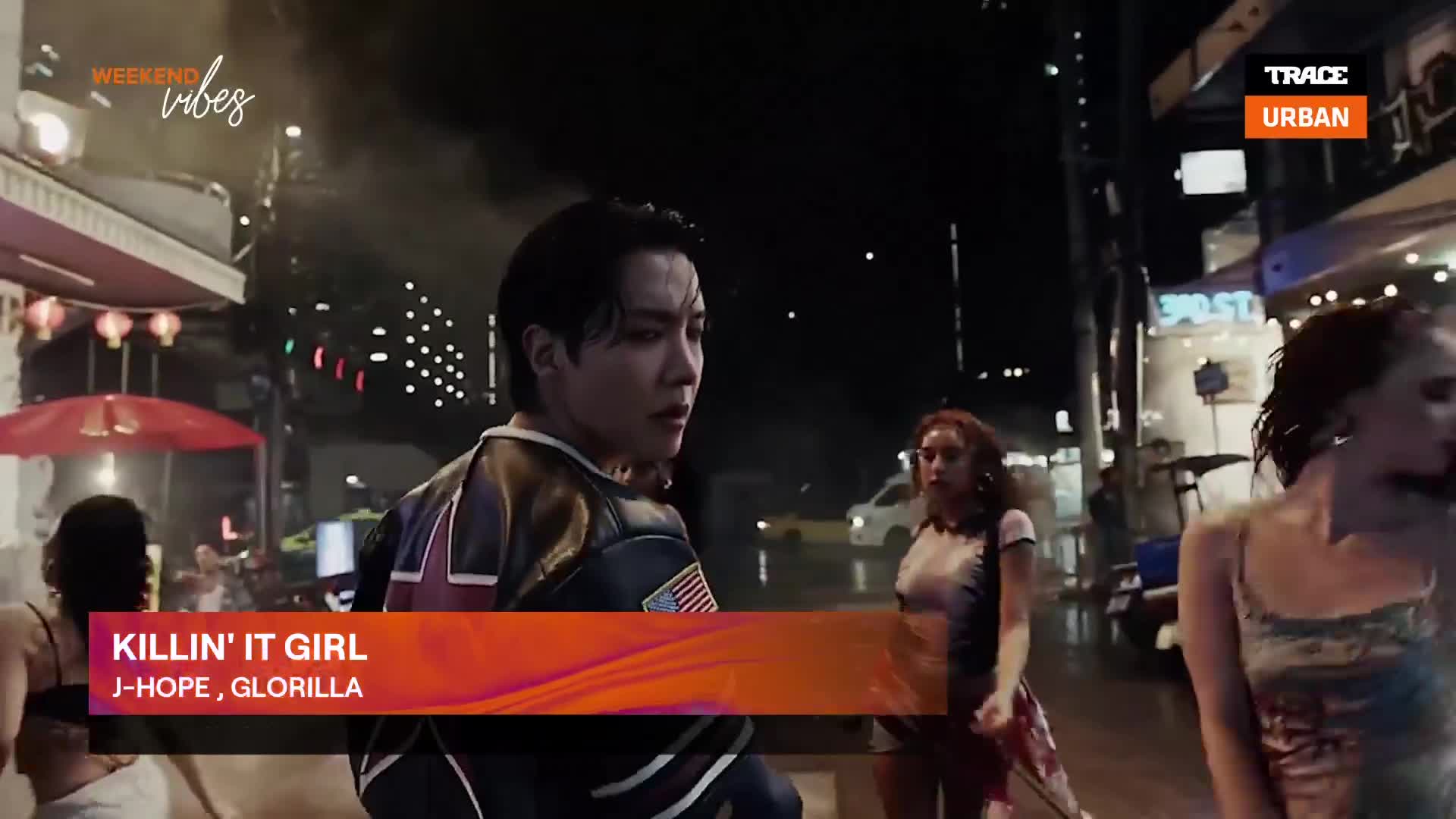 A man in a bomber jacket looks over his shoulder as he walks down a neon-lit street. Women stroll past, and the Trace Urban logo is in the corner.
