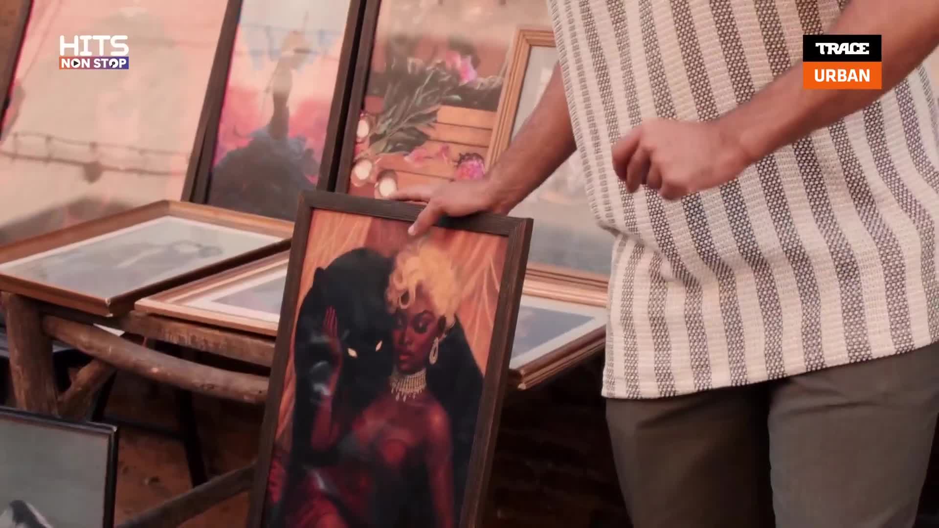 A man in a striped shirt is holding a framed piece of art, displaying it for the camera. The artwork depicts a woman and a black panther, with other framed pieces visible in the background.
A man in a striped shirt is holding a framed piece of art, displaying it for the camera. The artwork depicts a woman and a black panther, with other framed pieces visible in the background.