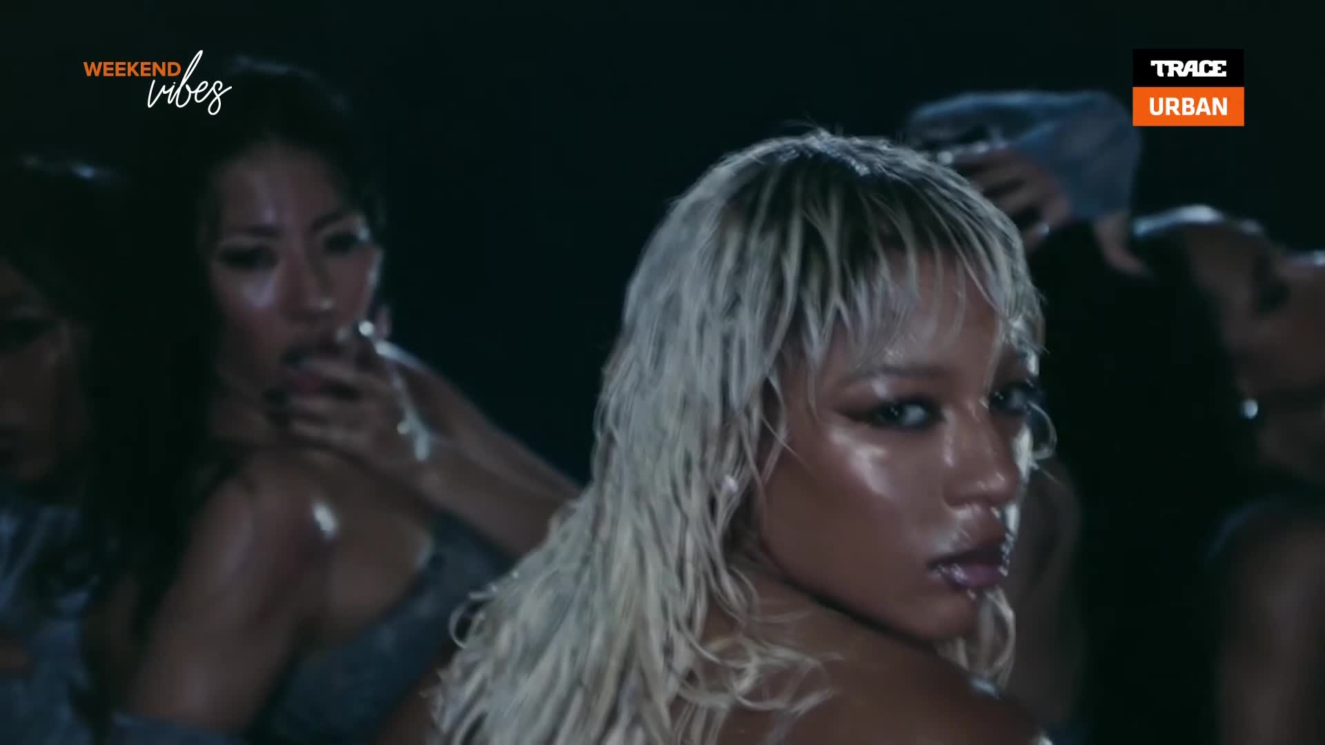 The blonde woman's wet hair clings to her face as she turns, her eyes catching the light. Behind her, another woman, her face slick with sweat, brings a cigarette to her lips. The blonde woman's wet hair clings to her face as she turns, her eyes catching the light. Behind her, another woman, her face slick with sweat, brings a cigarette to her lips.