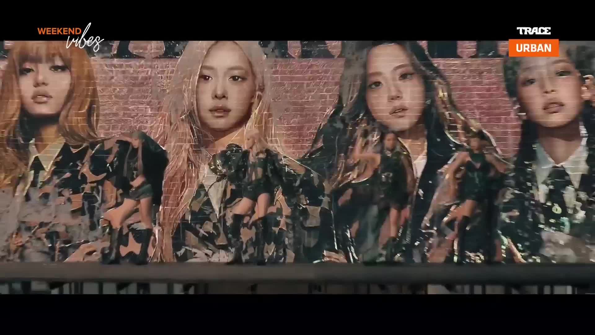 Four women stand behind a railing, their faces illuminated against a brick backdrop. They wear matching camouflage jackets, their expressions serious as they look forward. Four women stand behind a railing, their faces illuminated against a brick backdrop. They wear matching camouflage jackets, their expressions serious as they look forward.