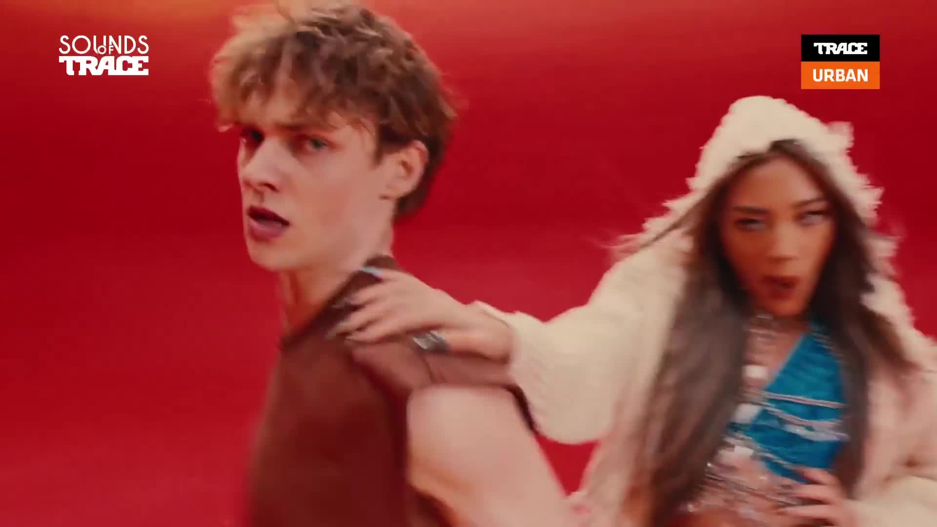 A young man with tousled hair turns his head, his mouth open as if speaking. A woman in a fluffy white hooded jacket reaches out, her hand resting on his shoulder. A young man with tousled hair turns his head, his mouth open as if speaking. A woman in a fluffy white hooded jacket reaches out, her hand resting on his shoulder.