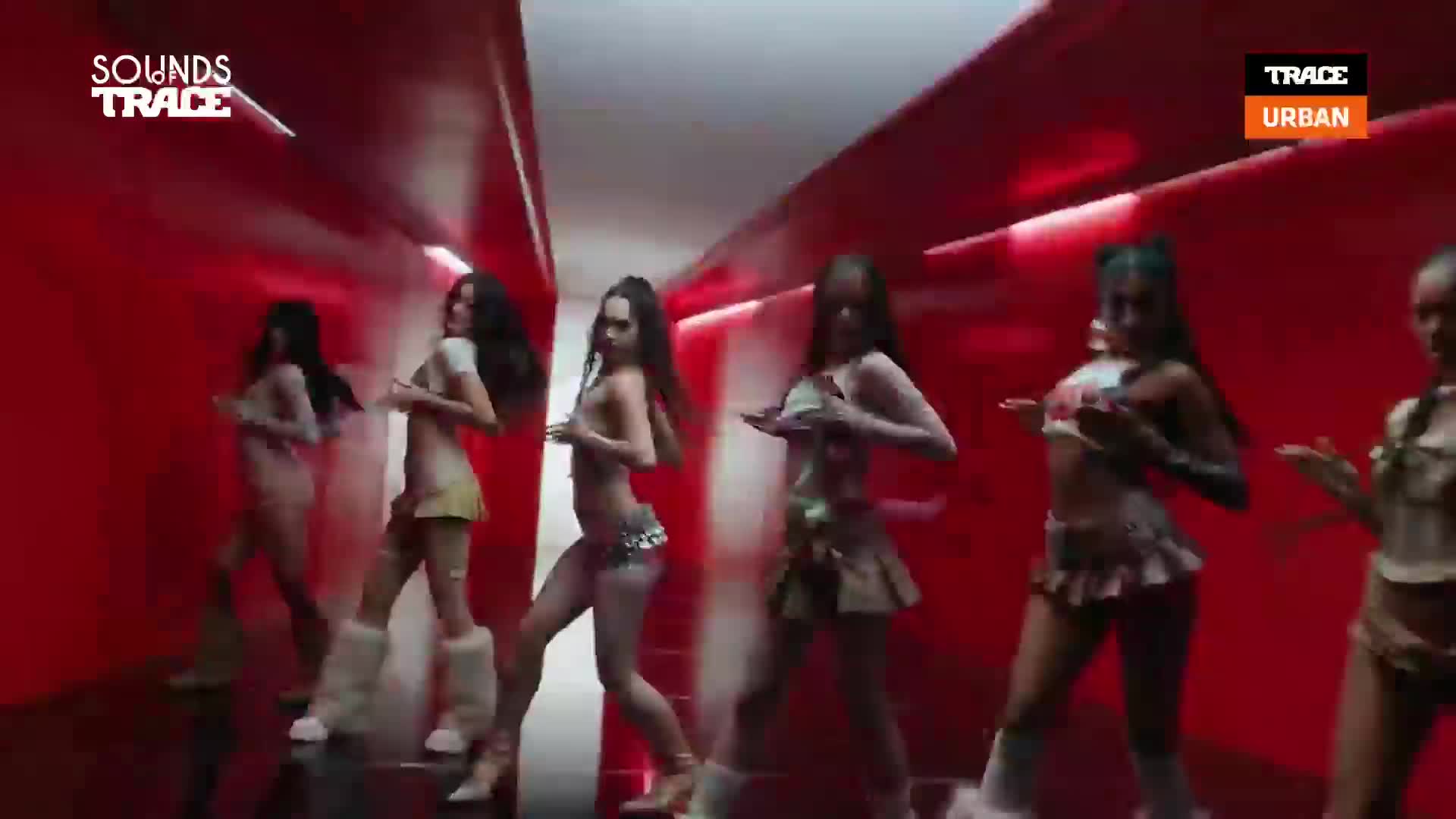 A group of women move in unison down a red, futuristic hallway. Their coordinated steps and gestures suggest a choreographed performance for Trace Urban.