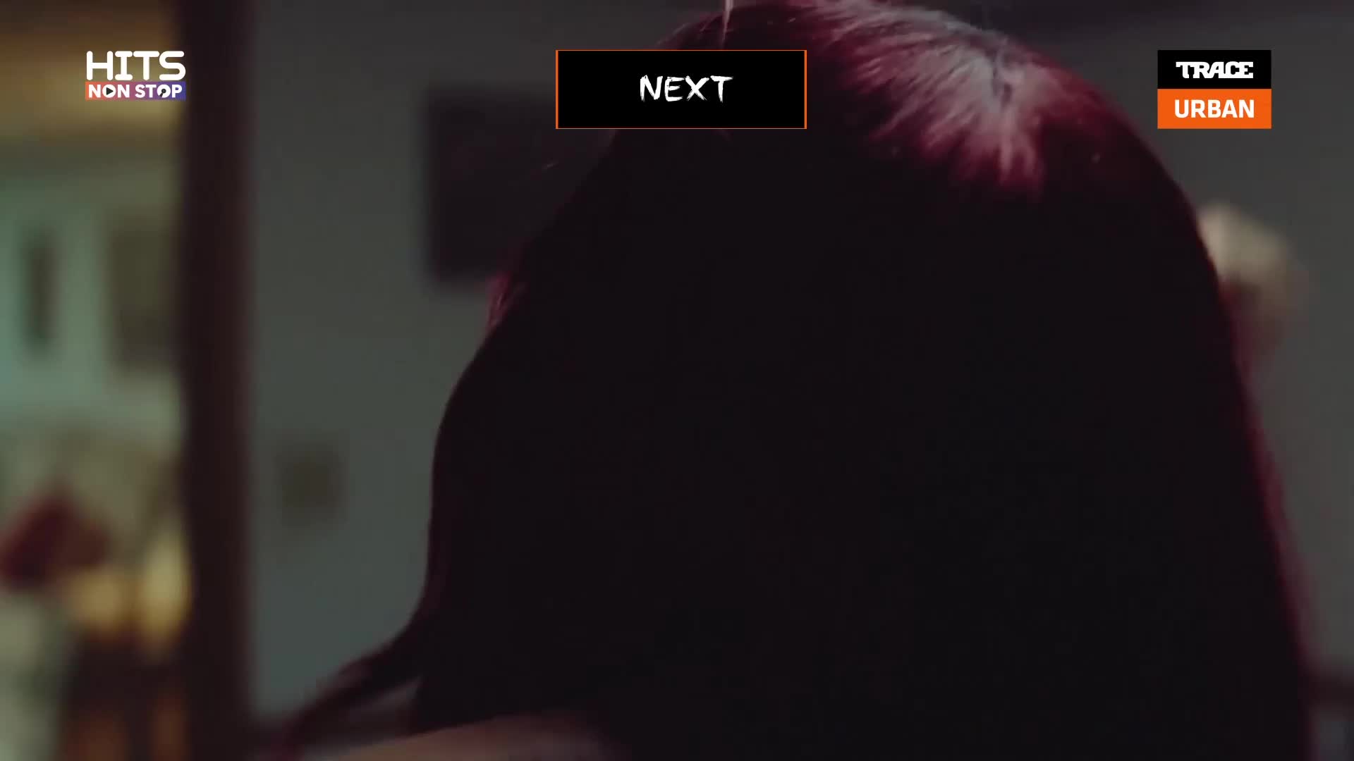 A dark-haired person is turning their head, revealing a glimpse of a blonde person behind them. A "NEXT" button hovers over the dark-haired person's head, with "HITS NON STOP" and "TRACE URBAN" logos visible on the left and right.