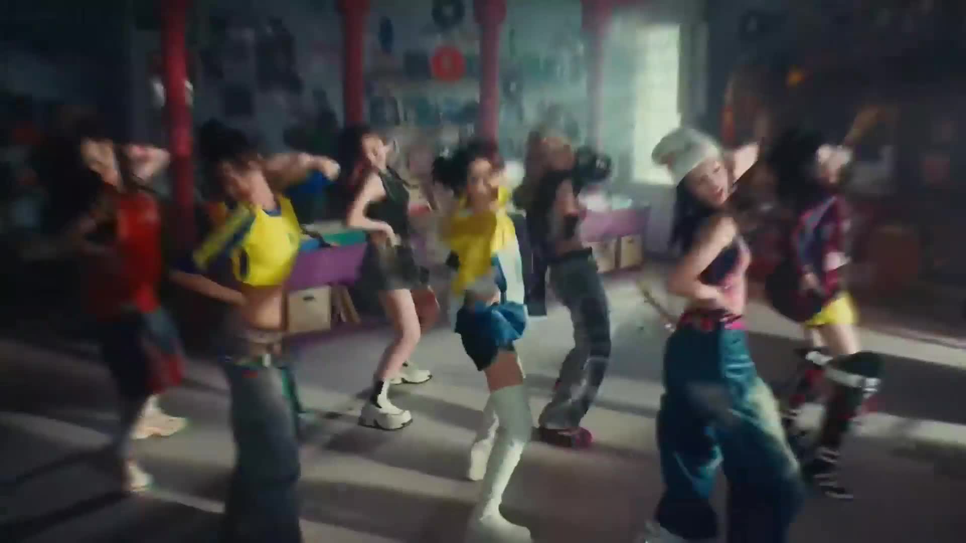 A group of young women in vibrant, baggy streetwear are dancing in unison. Their movements are sharp and synchronized, a dynamic display against a backdrop of what looks like a Parisian loft.