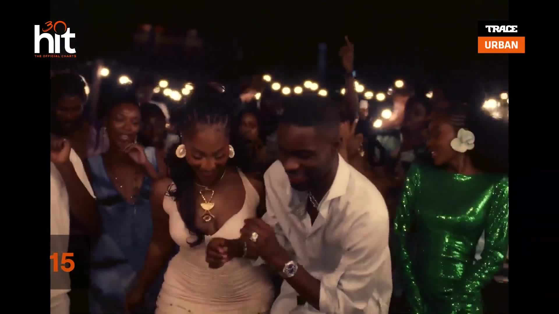 A couple dances closely under string lights, a Trace Urban party in full swing. The woman in front, wearing a light dress, sways with her partner, while others move to the music behind them.