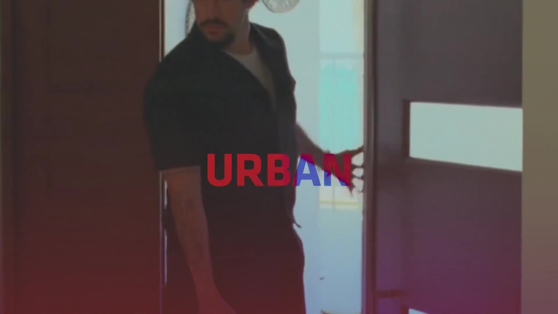 A man in a dark shirt pushes open a door, his hand gripping the edge. The word "URBAN" flashes across his chest in bold red and blue letters. A man in a dark shirt pushes open a door, his hand gripping the edge. The word "URBAN" flashes across his chest in bold red and blue letters.