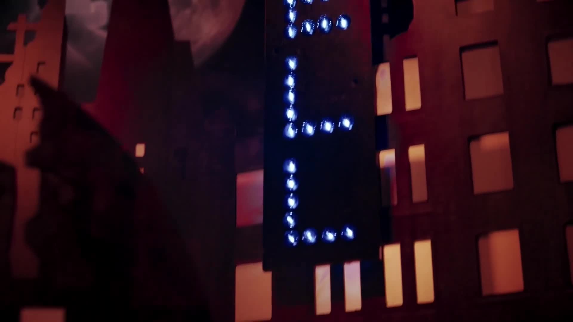 A dark, stylized cityscape looms, with a vertical sign of blue lights forming the letter "E." Warm orange light spills from the windows of the buildings. A dark, stylized cityscape looms, with a vertical sign of blue lights forming the letter "E." Warm orange light spills from the windows of the buildings.