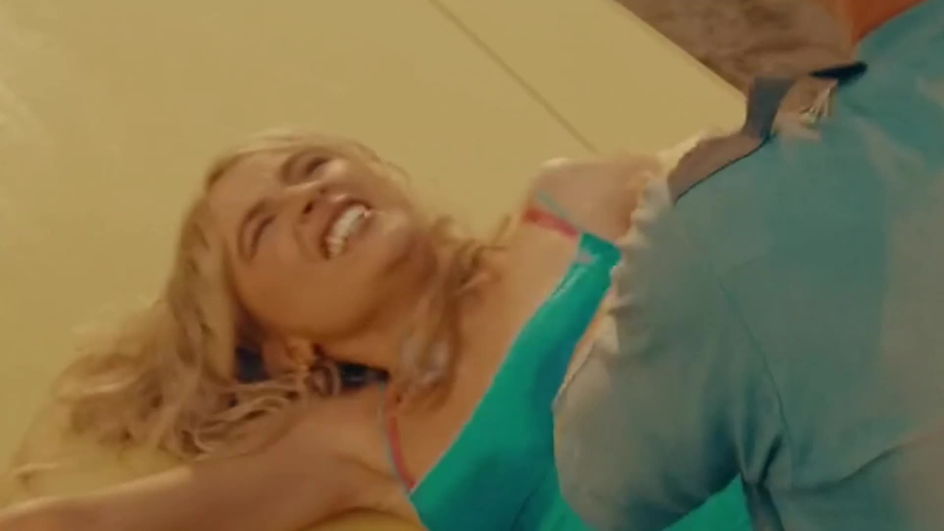 A woman with blonde hair is laughing, her head thrown back. She's wearing a bright teal dress as someone in a blue shirt leans over her. A woman with blonde hair is laughing, her head thrown back. She's wearing a bright teal dress as someone in a blue shirt leans over her.