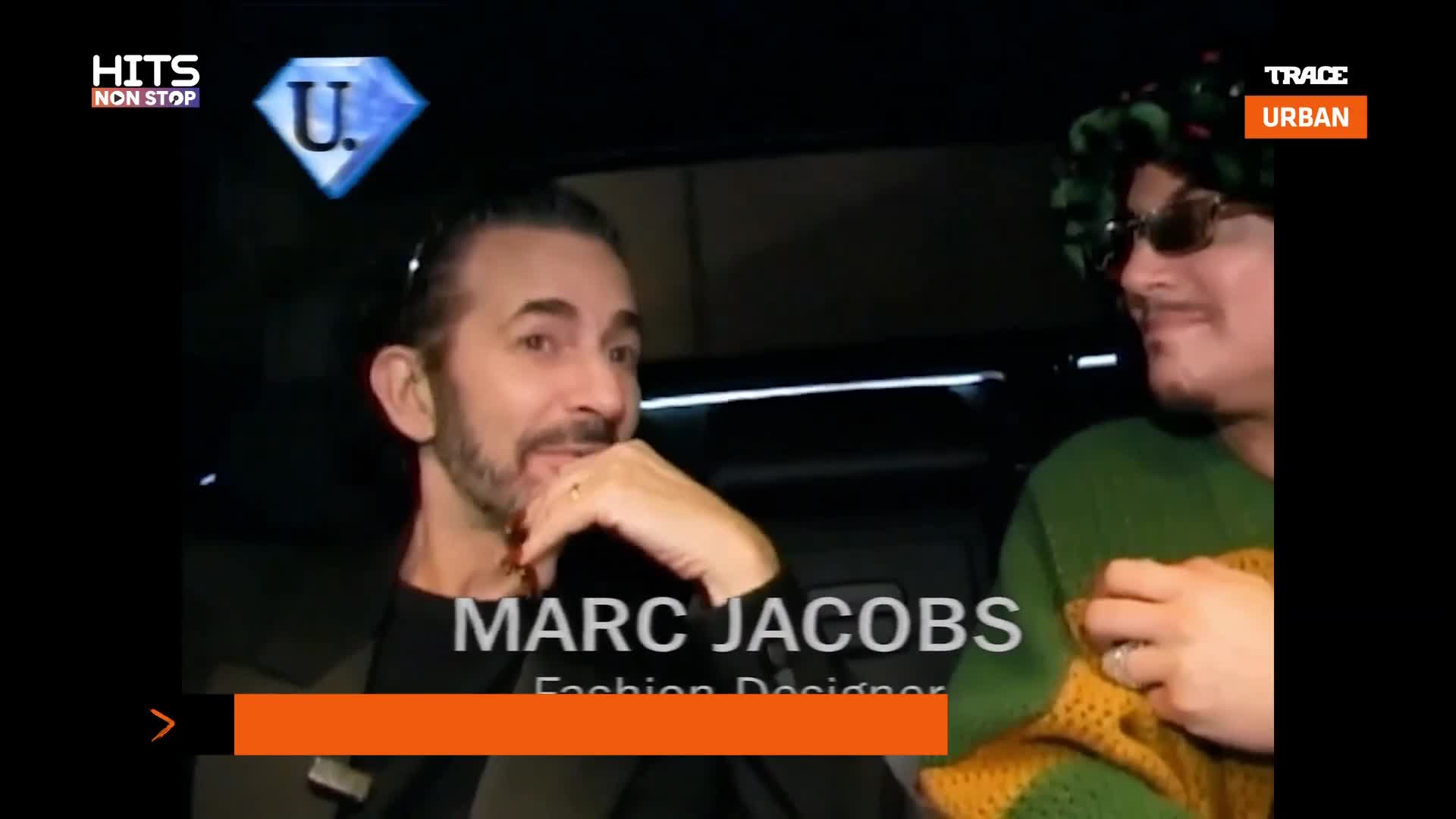 Marc Jacobs, a fashion designer, is speaking with someone wearing a green sweater and sunglasses. The Trace Urban logo is visible in the corner.
