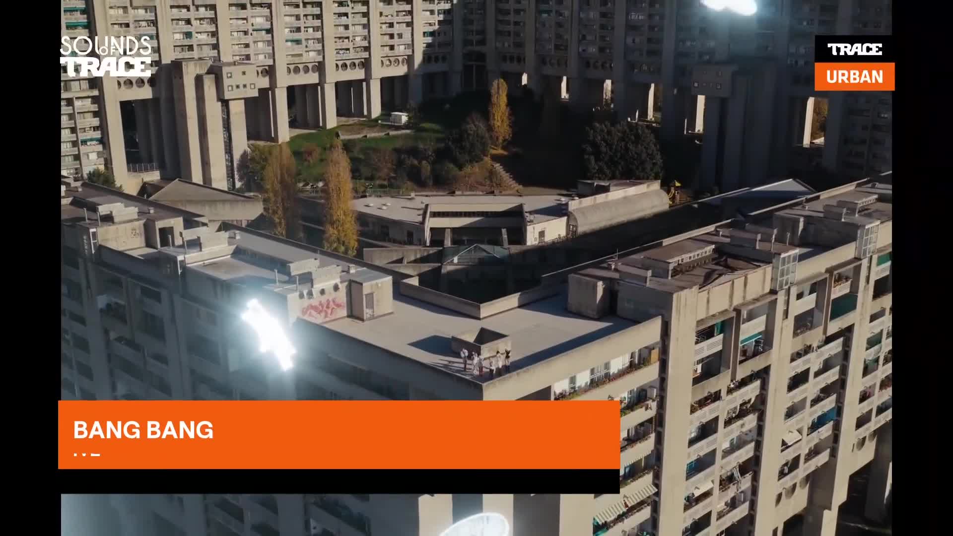 A group of people stand on the rooftop of a Brutalist building in France. The sun glints off a metal structure, illuminating the concrete facade.
