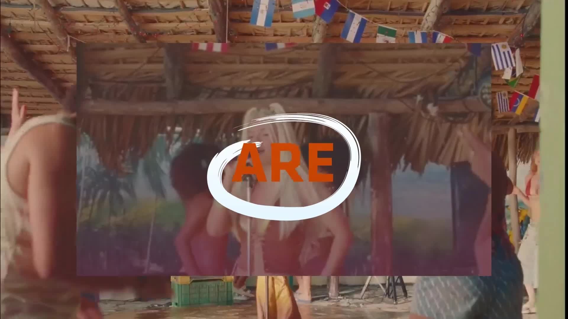 A woman with blonde hair sings into a microphone, her image framed by an orange circle with the word "ARE" inside. Flags from various countries hang above the thatched roof of a tropical structure.