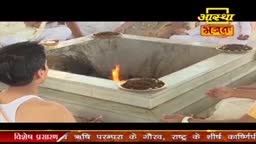 A small flame flickers inside a square, stone structure. People are gathered around, and small plates with dark offerings rest on the structure's edge.
