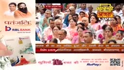 A crowd of people, likely in India, is gathered, some with hands clasped, as a live broadcast of Aastha Bhajan plays on a screen. To the left, a Patanjali RBL Bank advertisement shows a credit card with a peacock image.
