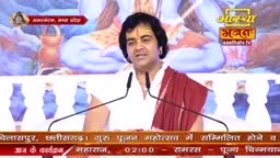 A man in a white shirt and a red shawl speaks into two microphones, his expression animated. The Aastha Bhajan logo is visible in the top right corner, and text at the bottom indicates a Guru Pujan Mahotsav in India.
