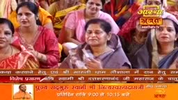 Women in colorful saris and shawls sit close together, their hands clasped or raised in what looks like prayer during an Aastha Bhajan broadcast from India. The camera focuses on the faces, capturing their expressions of devotion.
