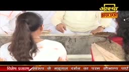 A woman with long dark hair looks towards a man in a cream-colored outfit. The Aastha Bhajan logo is visible in the top right corner.

