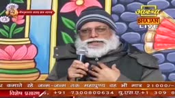 A man with a long white beard and a beanie speaks into a microphone, his hands gesturing towards his chest. The backdrop is a painted wall, and the "Aastha Bhajan LIVE" logo is visible.
