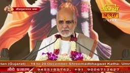 A man with a shaved head and glasses speaks into two microphones, a garland around his neck. Behind him, a backdrop of swirling colors frames the "Aastha Bhajan" logo.
