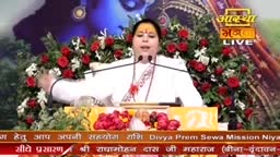 A woman in white speaks into two microphones, gesturing with her hands. Behind her, a floral arrangement of red roses and white flowers frames the set, and the Aastha Bhajan logo is visible.
A woman in white speaks into two microphones, gesturing with her hands. Behind her, a floral arrangement of red roses and white flowers frames the set, and the Aastha Bhajan logo is visible.