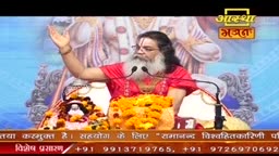 A man with a long white beard, wearing a bright red shirt, speaks into two microphones. He gestures with his right hand, palm open, as if addressing a crowd.