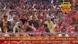 A large crowd is gathered, many wearing traditional Indian attire. Above them, a banner displays "Aastha Bhajan" in vibrant yellow and orange.