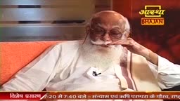 An elderly man with a long white beard and glasses rests his hand near his face. He wears a simple white garment, and a logo for "Aastha Bhajan" is visible in the background.