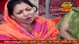 A woman in an orange sari speaks animatedly, her mouth open. Beside her, another woman in a green, patterned outfit listens.