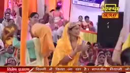 A woman in a yellow sari claps her hands, her face turned towards the front. Behind her, a crowd of people watches, some with their hands raised.