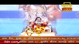 A man with a long white beard, adorned with garlands, sits on a raised platform. Behind him, a large image of a deity with a monkey-like face is visible.