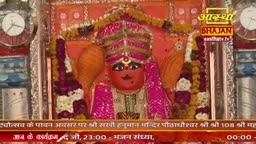 A vibrant idol of Hanuman, adorned with a jeweled turban and pink robes, stands at the center of a decorated shrine. A banner beneath displays Hindi text and the Aastha Bhajan logo.