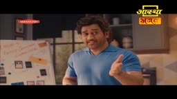 A man in a blue shirt gestures with his right hand, his thumb pointing upwards. Behind him, a whiteboard is covered in notes and diagrams, and a logo for Aastha Bhajan is visible.