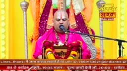A man in a vibrant pink robe speaks into a microphone. Behind him, a silver mace stands tall against a backdrop of yellow and purple fabric.