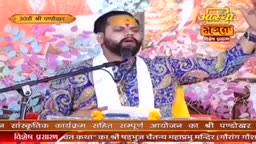 A man with a tilak on his forehead sings into a microphone, his eyes closed in devotion. He wears a vibrant, patterned kurta and a white scarf.