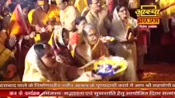 A woman in a light sari holds a plate of offerings, her eyes focused ahead. The crowd around her, dressed in bright yellow and white, is a sea of devotional faces.