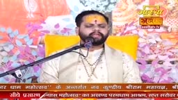 A man in traditional Indian attire sits before a microphone, his eyes closed in prayer. Behind him, a vibrant yellow cushion and floral backdrop frame the scene.