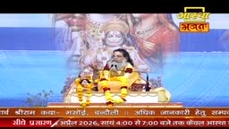 A man with a long beard sits on a raised platform, draped in yellow and adorned with marigold garlands. Behind him, a large image depicts Hindu deities. A banner at the bottom of the screen displays text in Hindi.