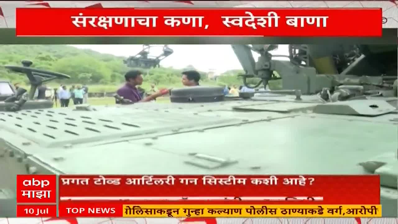 Two men stand atop a large, olive-green artillery gun, likely discussing its mechanics. A news segment from ABP Majha, with text in Marathi, highlights the system.
