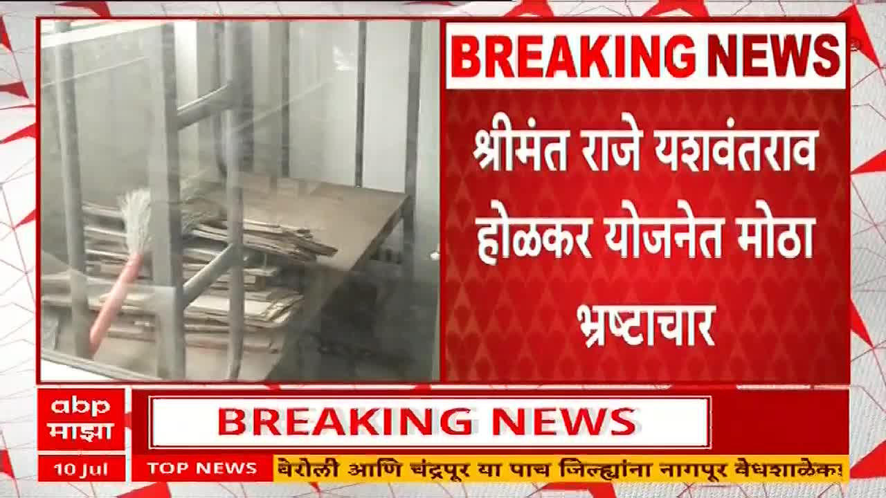 Behind the ABP Majha logo, a brush rests against a metal grate, next to a stack of cardboard. The screen displays "BREAKING NEWS" about alleged corruption in the Holkar Yojana.
