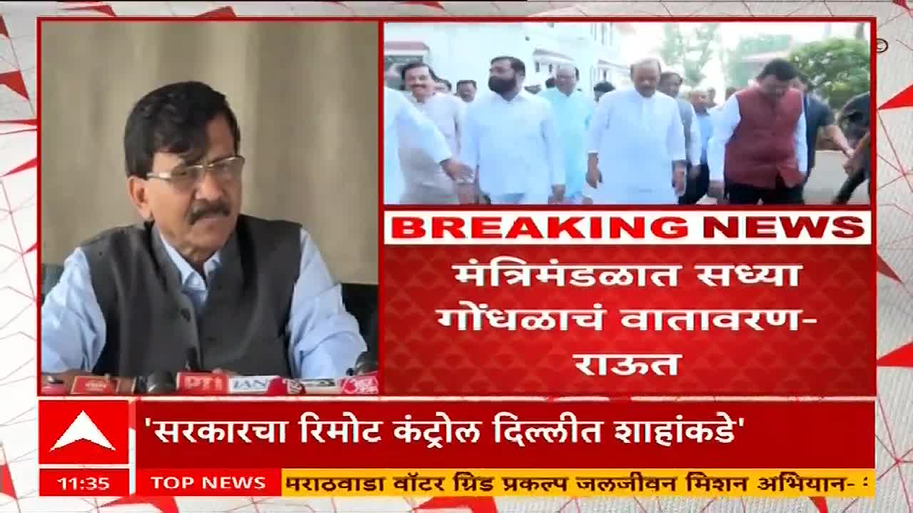 A man in glasses speaks intently on ABP Majha, while a group of men in white shirts walks in the background. The screen flashes "BREAKING NEWS" in Marathi, with a headline about the cabinet.
