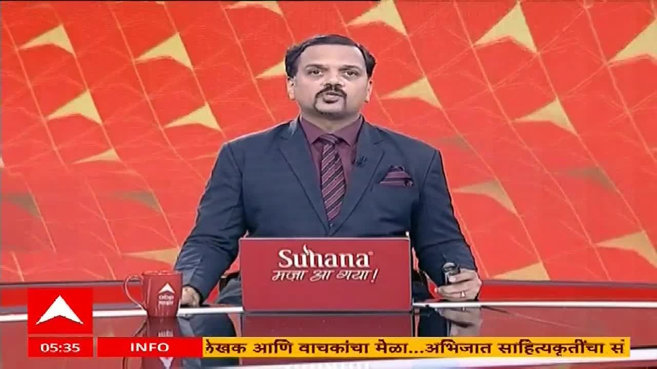 The ABP Majha news anchor, in a dark suit and tie, is speaking directly to the camera from a studio set. A mug with the ABP Majha logo sits on the desk in front of him.
