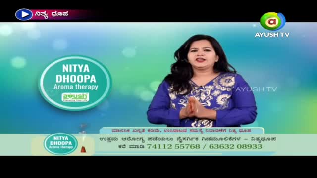 A woman in a blue top stands in front of a screen for Ayush TV, speaking with her hands clasped. The graphic behind her advertises "Nitya Dhoopa Aroma therapy."
