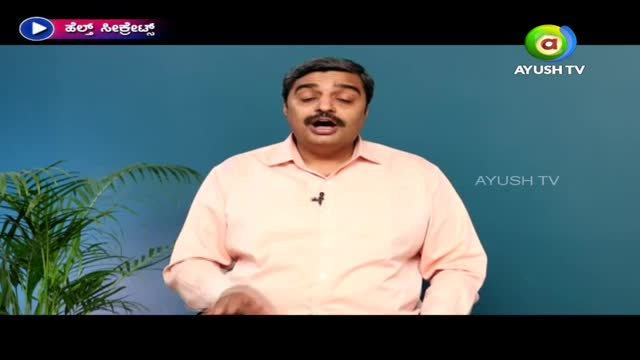A man in a pink shirt is speaking, a small microphone clipped to his collar. The Ayush TV logo is visible, and a plant sits to the side.
